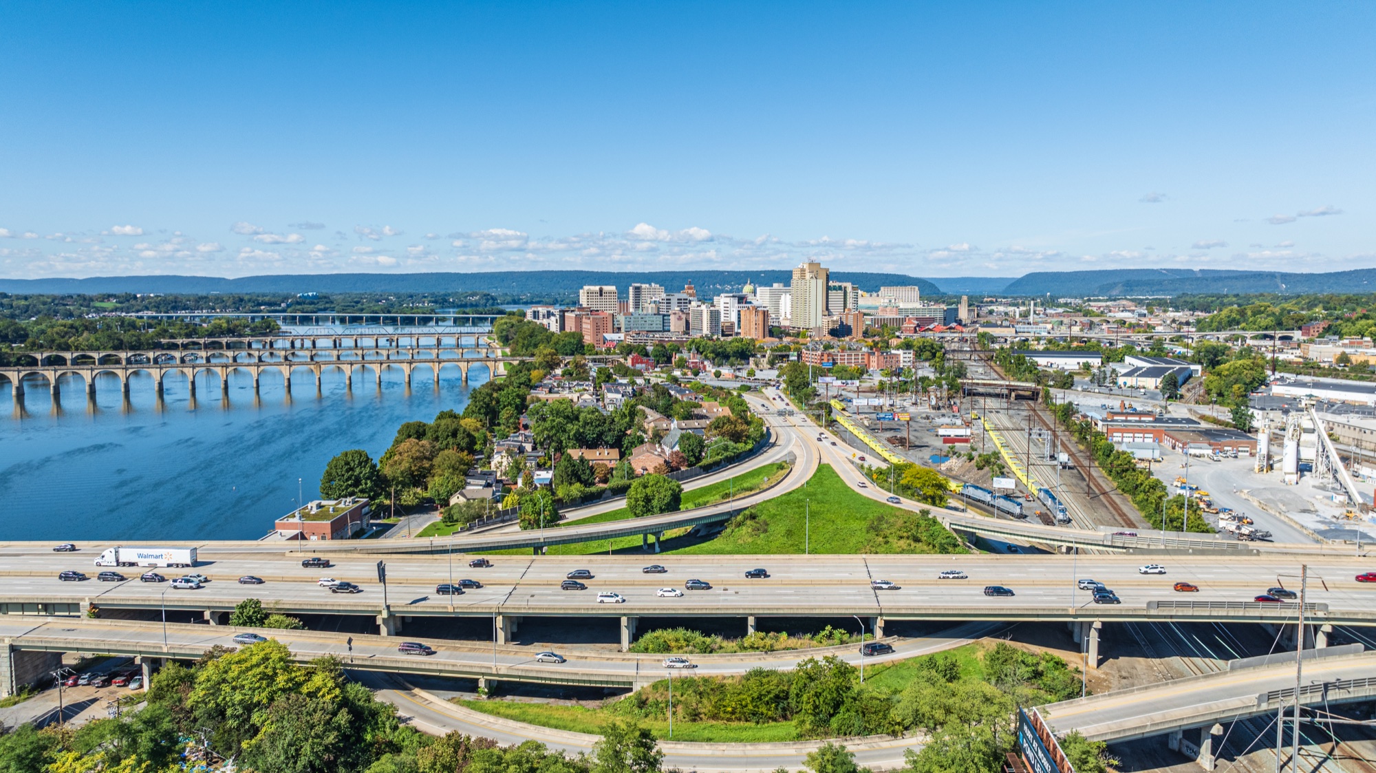 Aerial view across the Susquehanna River, highway, rail corridor, and bridges toward downtown Harrisburg